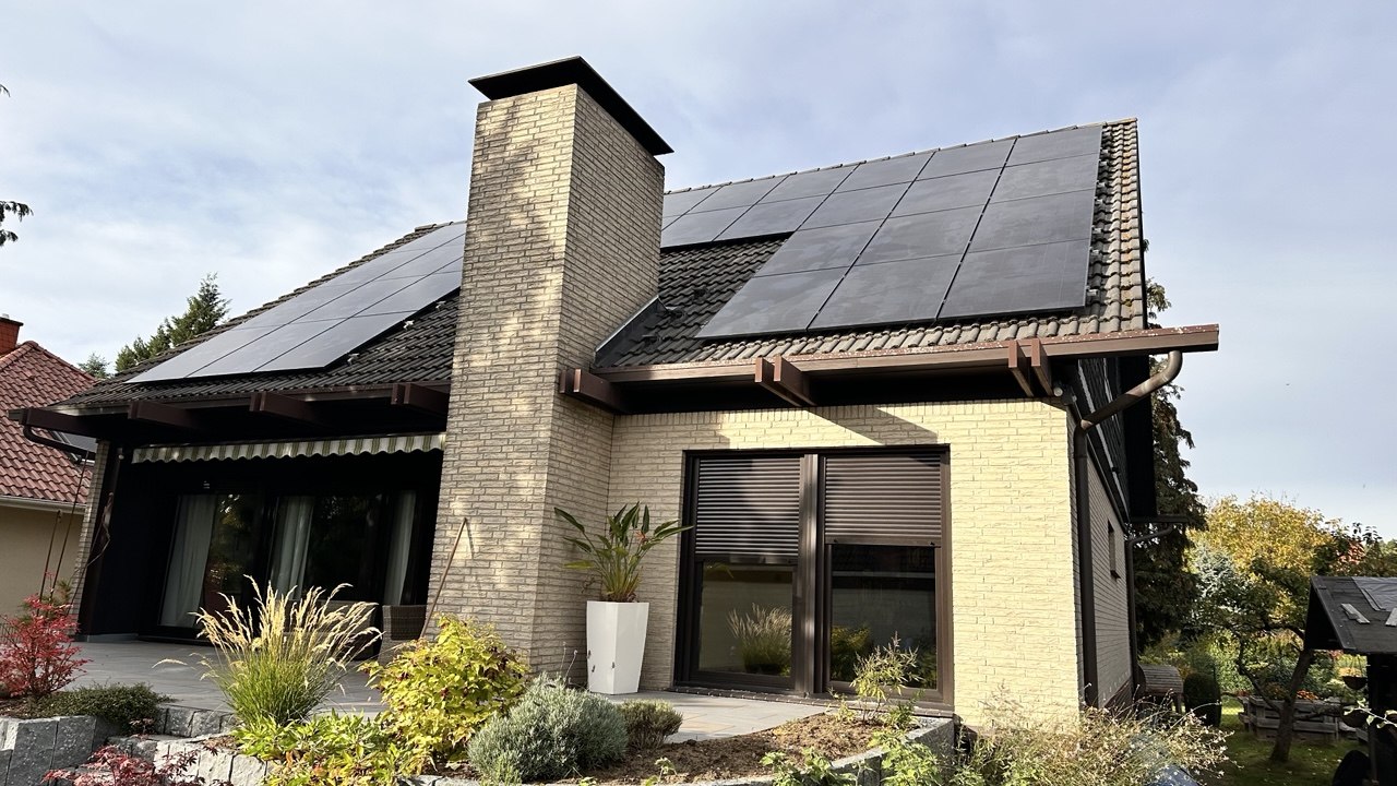 Einfamilienhaus mit gelbem Klinker, schwarzer PV-Anlage auf dem Satteldach und einer Pergola an der Terrasse